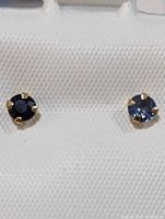 Close-up front view of a pair of 10K yellow gold stud earrings with round blue sapphire gemstones mounted on prong settings