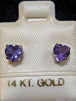 Front view of earrings on white holder marked '14 KT. GOLD' showing heart-shaped purple gemstones.