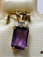 Close-up of the pendant showing the purple amethyst and the small white gemstone above it in 14K yellow gold setting.
