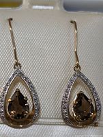 Front view of pair of pear-shaped smokey topaz earrings surrounded by small clear stones on teardrop-shaped frames in 14K yellow gold.