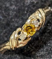 Close-up front view of 10K gold ring with a bright round yellow labgrown diamond center stone and two smaller white diamond side stones on a textured surface.