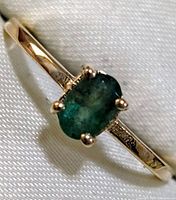 Top angle view of ring showing oval green emerald center stone and part of band.