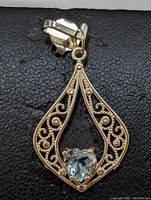 Front view of the gold pendant showing the heart-shaped blue topaz in the center with decorative gold filigree around the pendant