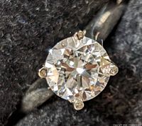 Close-up of round brilliant center diamond in four-prong setting with small accent diamonds on prong tips against black fabric