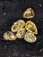 Close-up of six assorted baguette cut diamonds placed on black velvet showing variety of shapes and colors.