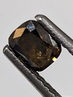 Close up detail of brown diamond held in tweezers showing facets and inclusions.