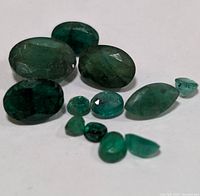 Close-up photo of 11 various loose emerald gemstones in different shapes and sizes showing natural inclusions.