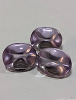 Three polished oval amethyst gemstones arranged closely on a plain light background, showing front faces with high translucency and light purple hues.