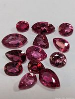 Photo showing 13 loose pink tourmaline gemstones of various cuts and shapes on white background.