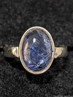 Close-up image of sterling silver ring with oval cabochon tanzanite stone on black fabric, showing gemstone clarity and setting.