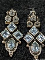 Front view of pair of sterling silver earrings with aquamarine gemstones set in geometric pattern.