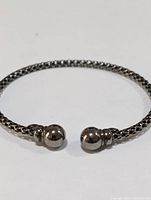 Sterling silver open cuff bracelet viewed close-up showing textured woven band and rounded end caps.