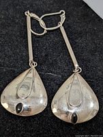 Pair of sterling silver dangle earrings with teardrop-shaped pendants and black stones on a black background.