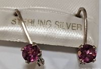 Close-up front view of pair of sterling silver earrings with red garnet stones, showing 'STERLING SILVER' tag.