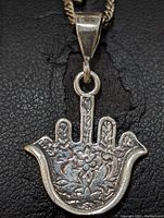 Close-up front view of sterling silver Hamsa hand pendant necklace showing floral engravings and textured details on black textured background.