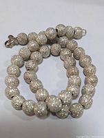 Full view of the textured bead necklace showing round silver beads with granular texture and lobster clasp.