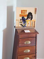 Square carnival mirror with Ozzy Osbourne graphic and headless executioner theme on top of wooden drawer chest.