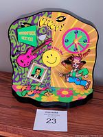 Front angled view of retro 1960s Hoffman animated clock showing colorful groovy and flower power design with guitar, Woodstock sign, smiley face, and dancing figure.