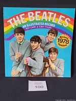 Front cover of 'The Beatles' illustrated record book showing four Beatles in gray suits with a rainbow and title text