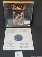 Front view of The Doors Live at the Hollywood Bowl laserdisc in shrink wrap, showing Jim Morrison image on sleeve and disc media in paper sleeve.