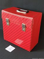 Front view of the vintage vinyl record case showing red vinyl with white diagonal stripes, locking latches, and top handle.