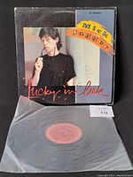 Front view of the vinyl single "Lucky in Love" by Mick Jagger with sleeve and translucent protective plastic on table, light wear visible on sleeve edges.