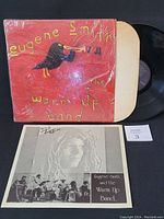 Front cover of the vinyl record, red with bird graphic and vinyl partially visible outside sleeve. Signed inner insert and a small number card placed in front.