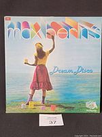 Front cover of Max Berlin's Dream Disco vinyl record showing a woman painting the sky with paint cans on grass near water.
