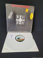 Front of vinyl record and sleeve, with shrink wrap intact showing yellow price sticker and cut/dent damage on corners.