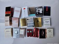 Lot of approximately 20 assorted perfume and cologne sample packets including many designer brands laid out on white background.