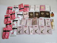 Assorted perfume samples laid out on white surface showing pink sachets of Victor & Rolf Bonbon, multiple Scandal sachets and mini bottles, and other boxed perfume samples.