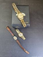 Photo showing three vintage women's watches on black background: a Pulsar watch on its box with gold linked band, a gold expansion band watch, and a small square watch with brown leather strap.