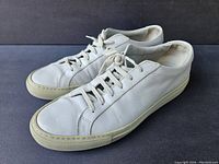 Pair of men's white leather sneakers, angled front-left side view showing overall design and condition.