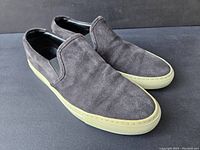 Pair of grey suede slip-on Common Projects shoes shown at a 3/4 angle eliminating one shoe's side view.