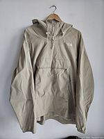Front view of beige hoodie jacket with front pouch pocket and hood on hanger