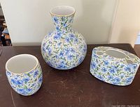 Three porcelain floral patterned items: round vase, small cup, and floral frog.