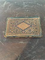 Top side of antique embossed leather billfold showing a central diamond pattern and floral motifs with signs of wear and scratches.