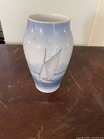Front view of Royal Copenhagen porcelain vase showing hand-painted sailboat on water with blue gradient background.