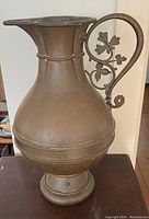 Side view of the large copper pitcher showing the floral design handle and decorative engravings
