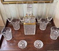 Full set of crystal glassware including the decanter with stopper, tall and small glasses arranged on wooden surface