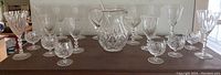 Full set of assorted crystal glassware arranged on a wooden surface including glasses and a pitcher