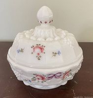 Front angle of Fenton ladies powder dish showing floral design, embossed grape cluster and leaves, and finial knob.