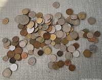 Coins scattered on a fabric surface showing various sizes and metallic tones, including silver, bronze, and gold-like colors.