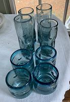 Tall and short blue-green handblown glasses with textured surfaces and bubbles inside glass.
