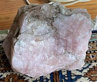 Side view of large rough rose quartz stone showing pink and white coloration and natural texture.