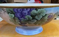 Side view showing the hand-painted grapes and grape leaves with gold rim and light blue foot.