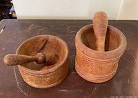 Both wooden mortar and pestle sets placed side by side on a table, showing overall size and condition with visible wear.
