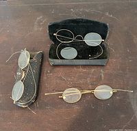 Three pairs of antique spectacles displayed with two black cases on a wooden surface.