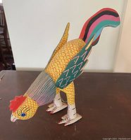 Front angled view of the colorful wooden chicken figurine standing on a brown surface.