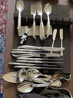 Full view of assorted silverplate flatware laid out on wooden rack showing spoons, forks, knives, and serving utensils.